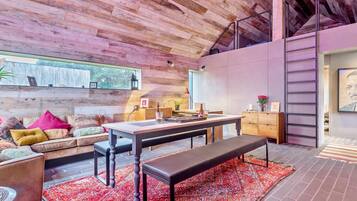 A modern interior with a wooden ceiling, a dining area with a bench, a sofa with cushions, and a small table with a bottle.
