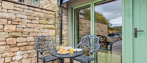 A stone wall, a green door, and a table with chairs and croissants.