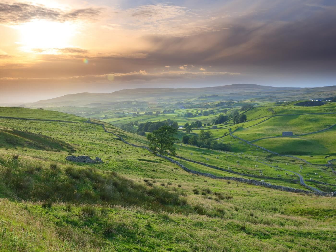 Rolling green hills, stone walls, and a clear sky.
