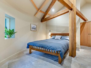 Ein Schlafzimmer mit hölzernem Bettgestell, einem Fenster mit Pflanze, einem gerahmten Bild an der Wand und einem Holzschrank.