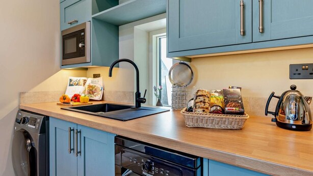 A modern kitchen with blue cabinetry, a built-in microwave, a kettle, and a bread basket. - 1 Bed in Kirkby Stephen (oc-95627) (Ravenstonedale)