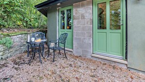 A building with a stone wall, green doors, and a patio with a table and chairs. - 1 Bed in Kirkby Stephen (oc-95627) (Ravenstonedale)