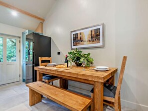 A dining area with a wooden table, chairs, a bench, a potted plant, and a framed picture on the wall.