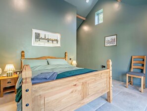 Ein Schlafzimmer mit einem hölzernen Bett, zwei Nachttischen mit Lampen, einem Sessel und zwei gerahmten Bildern an der Wand.