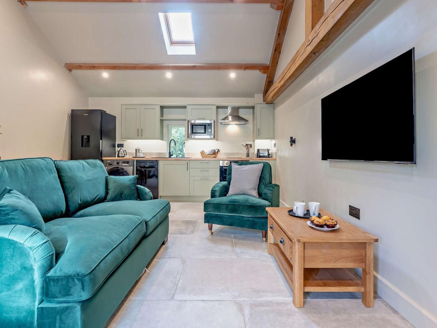 Una sala de estar moderna con un sofá azul turquesa, una mesa de centro de madera y una cocina al fondo.