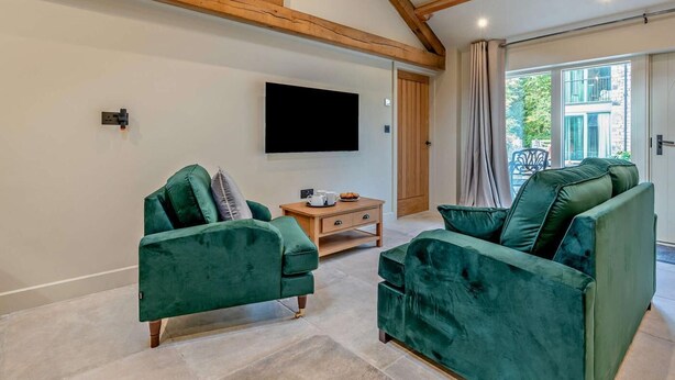 Um quarto com dois sofás de veludo verde, um armário de madeira, uma televisão de tela plana e uma janela grande com cortinas.