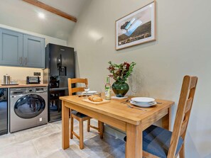 A compact kitchen with a washing machine, a refrigerator, and a dining area with a table set for two. - 1 Bed in Kirkby Stephen (oc-95629) (Ravenstonedale)