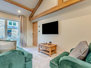 A living room with a television mounted on the wall, a wooden coffee table with a kettle and cups, and two green sofas.