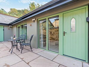 A patio with a table and chairs, a green door, and a stone wall. - 1 Bed in Kirkby Stephen (oc-95629) (Ravenstonedale)