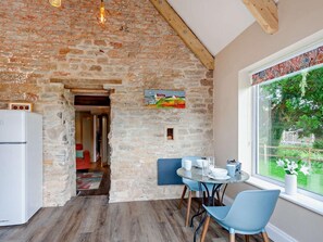 A rustic kitchen with exposed brick walls, a wooden ceiling, and a dining area with a table and chairs. - 1 Bed in Wedmore (oc-95582) (Theale)
