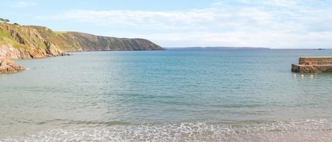 Une plage côtière, avec un ciel dégagé, une mer calme et une falaise rocheuse.