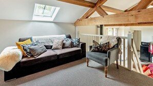 Ein Loft-Zimmer mit freiliegenden Holzbalken, einer Couch mit gemusterten Kissen, einem Sessel und Blick auf eine Treppe.