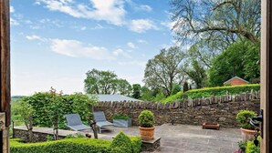 Eine Terrasse mit Steinmauern, einem Kiesweg und Blick auf einen Hügel mit Bäumen.