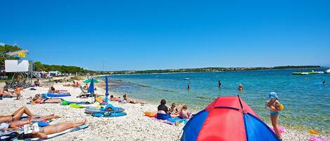 Ein Strand mit badenden Personen, einem Zelt und Booten im Wasser.