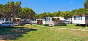 A row of mobile homes with a grassy yard, a fire hydrant, and a car parked in front. - Campinghomes (Medulin)