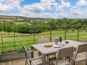 An outdoor dining area with a table set for two, overlooking a green landscape with sheep grazing. - 1 Bed in Hereford (oc-42897) (Craswall)