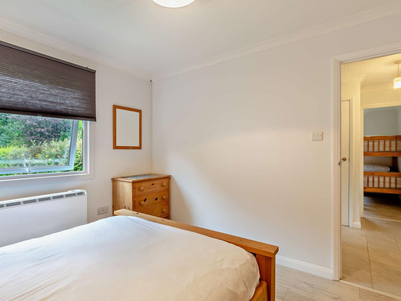 A bedroom with a bed, a dresser, a window with blinds, and a door leading to a bunk bed area.