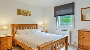 A bedroom with a wooden bed, bedside lamps, a radiator, a window with a view, and a dresser. - 2 Bed in Saltash (oc-95642) (Notter)