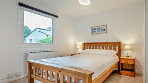 Een slaapkamer met een houten bed, een raam met uitzicht, een nachtkastje met een lamp en een radiator.
