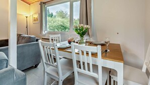 Een eetgedeelte met een houten tafel, witte stoelen, een bloemenvaas en uitzicht op groen buiten.
