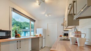Een moderne keuken met een groot raam, een magnetron, een koelkast en een houten aanrecht.