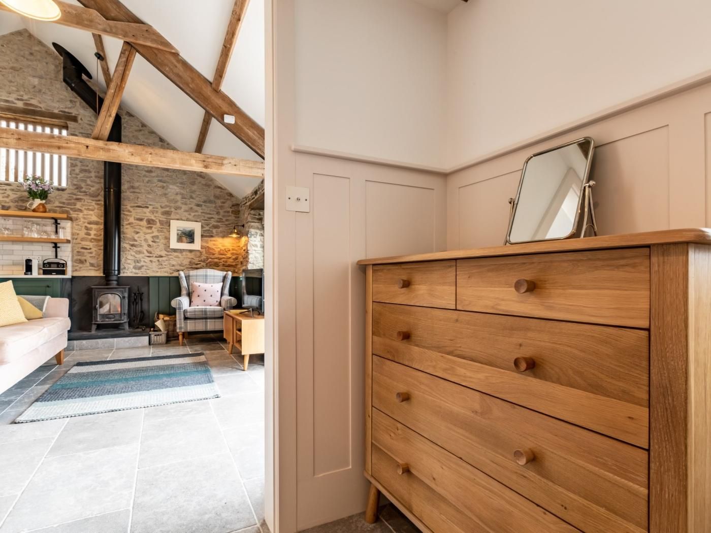 A cozy room with a fireplace, wooden dresser, and a stone wall.