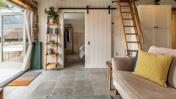 Ein gemütliches Zimmer mit einem Schlafplatz in der Esse, einer Holzleiter und einer Schiebetür im Bauernhausstil, die zu einem Flur führt.