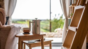Ein gemütliches Zimmer mit einem Holztisch, einer Metall-Kaffeekanne, einer Tasse und einem Stuhl.
