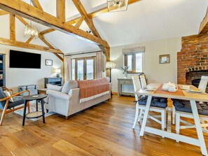 Ein gemütliches Wohnzimmer mit einer Couch, einem Esstisch mit Stühlen, einem Kamin und einem an der Wand befestigten Fernseher.