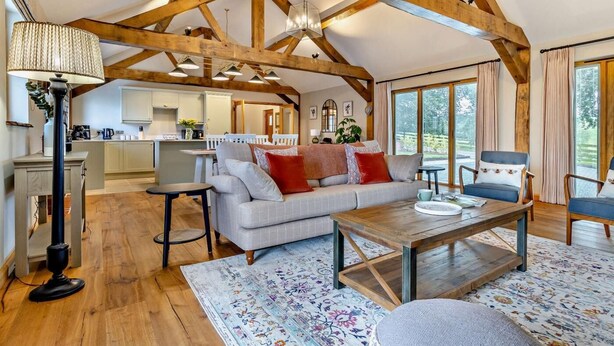 A spacious living area with a high ceiling, wooden beams, a sofa, a coffee table, and a view of the kitchen and outdoor space. - 1 Bed in Bromyard (oc-95609) (Pencombe)