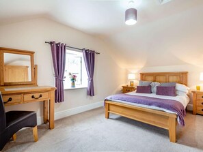 Ein Schlafzimmer mit einem hölzernen Bett, einem Schreibtisch, einem Stuhl und einem Fenster mit Vorhängen.