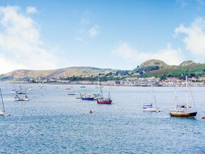 Eine Küstenstadt mit Booten auf dem Wasser, hügeligem Hintergrund und blauem Himmel.