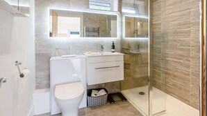Un baño moderno con cabina de ducha de vidrio, inodoro blanco, tocador con espejo y perchero.
