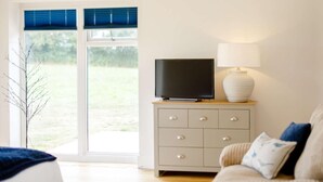 Un dormitorio con una cama, un televisor en una cómoda, una lámpara y vistas a un área verde por una ventana.