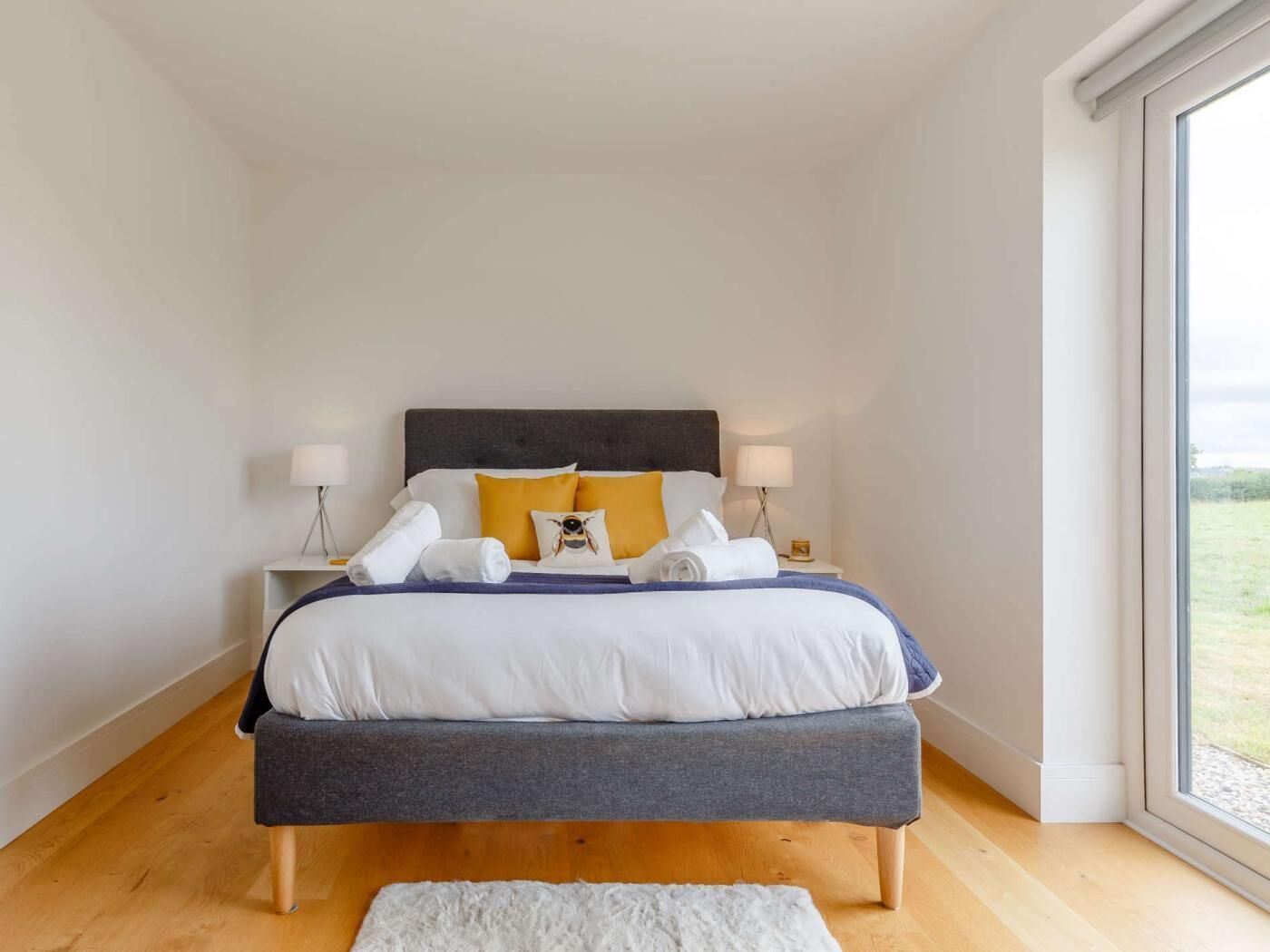 A bedroom with a bed, bedside lamps, a bench, and a view through a window.