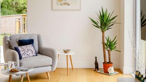 Un salón acogedor con un sillón gris, una mesita blanca, una planta en maceta y un cuadro en la pared.