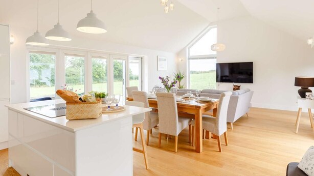 Cocina moderna con isla central, comedor con sillas y televisor montado en la pared.