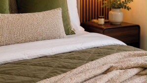 Ein ordentlich bezogenes Bett mit einer grünen Decke, einem weißen Kissen und einer gemusterten Tagesdecke.
