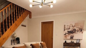 Ein Wohnzimmer mit einem Ecksofa, einer Holztreppe, einer Chandelüster und einer Tür.