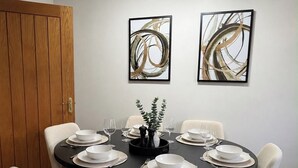 Ein Essbereich mit einem runden Tisch, gedeckt für sechs Personen, umgeben von sechs Stühlen, mit zwei abstrakten Gemälden an der Wand und einer Deckenleuchte darüber.