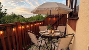 Eine Terrasse mit einem für vier Personen gedeckten Tisch, umgeben von Stühlen, unter einem großen Sonnenschirm.