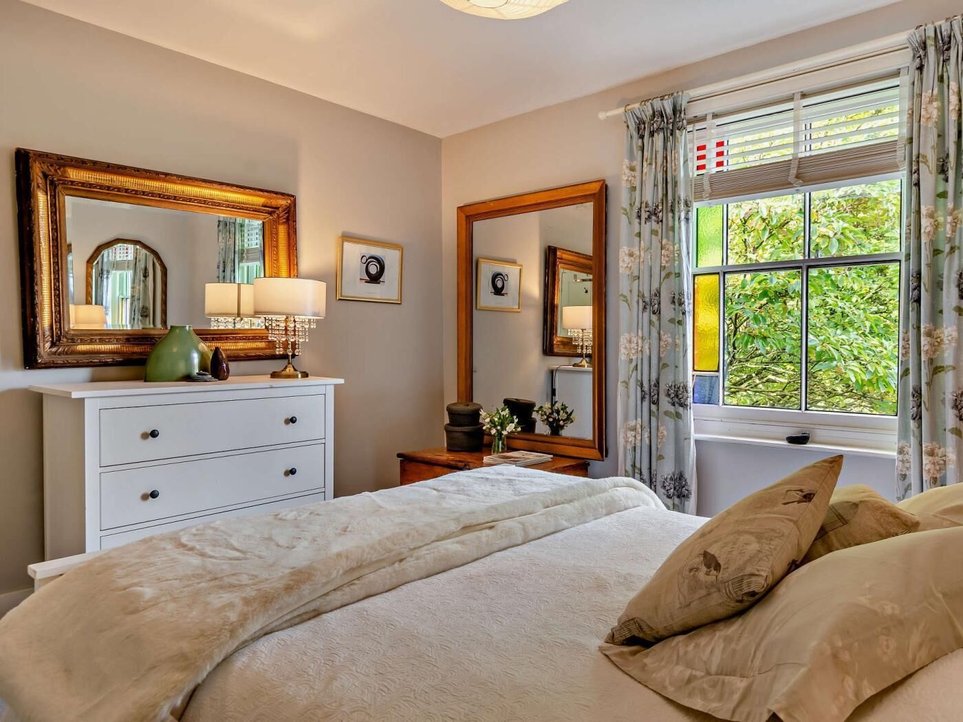 Ein Schlafzimmer mit einem Bett, einem Schminktisch, einem Spiegel und einem Fenster mit Vorhängen.
