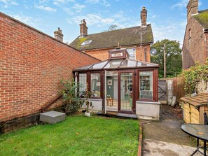 A conservatory with a glass roof, a brick wall, and a grassy yard. - 2 Bed in Lewes (oc-95692) (East Hoathly)
