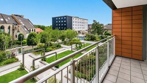 Un balcon donnant sur une cour, un immeuble à la façade moderne et un bâtiment traditionnel en pierre.