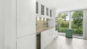Une cuisine moderne avec des meubles blancs, un four encastré et une grande fenêtre donnant sur un paysage verdoyant.