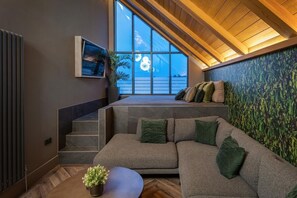 A modern interior with a sectional sofa, a small table, and a staircase leading to a balcony. - 4 Bed in Morpeth (oc-95713) (Amble)