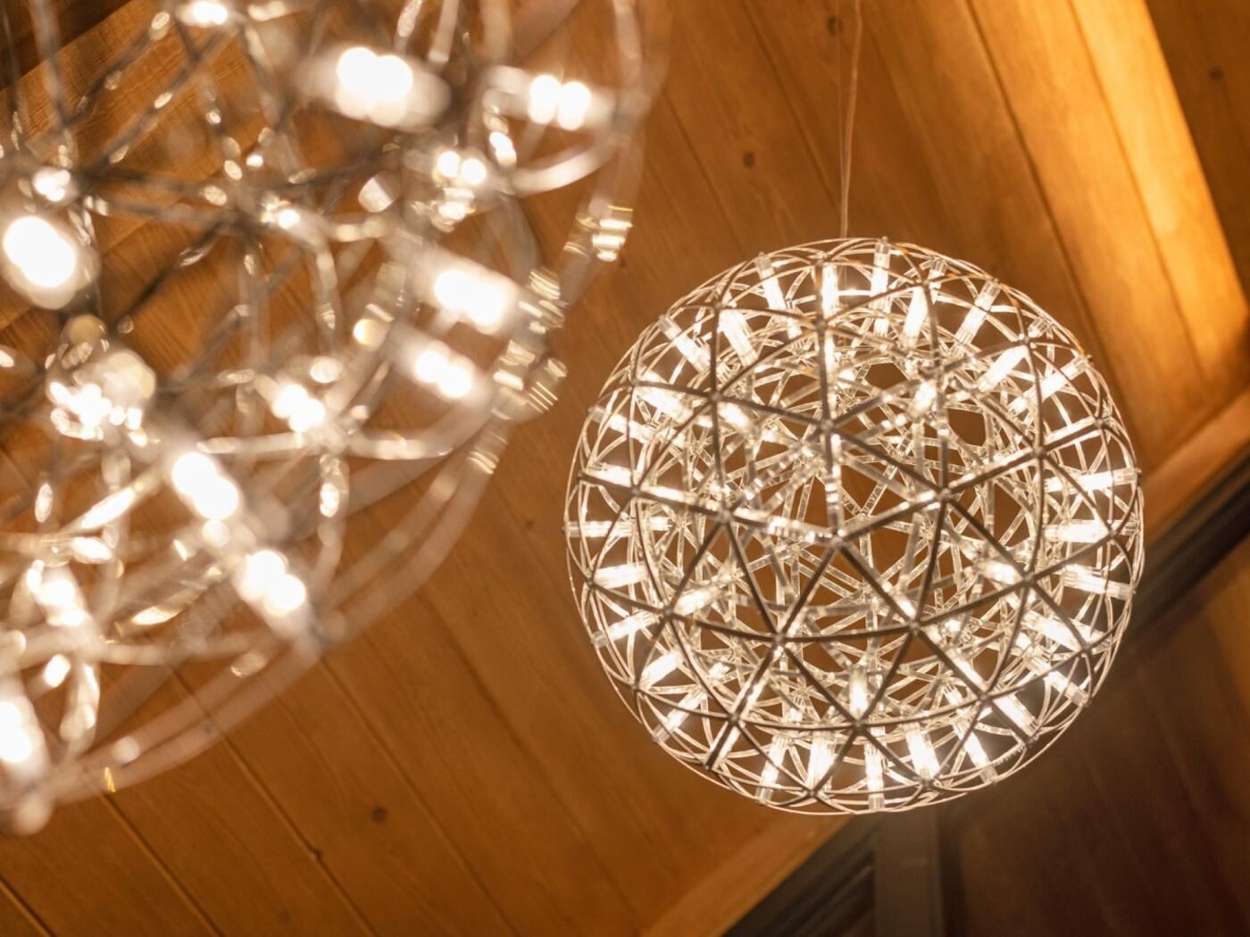 A spherical chandelier with a geometric design, hanging from a wooden ceiling.