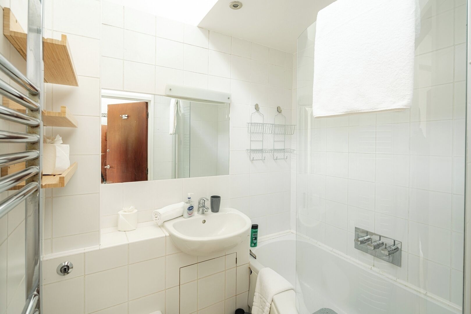A bathroom with a sink, mirror, towel rack, and shower area.