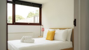 Um quarto com uma cama, uma janela, uma mesinha de cabeceira e um abajur.