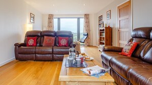 A living room with two leather sofas, a coffee table with items, and a bookshelf. - 5 Bed in Bideford (oc-76546) (Hartland)